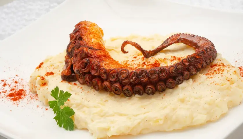 Delicioso pulpo a la plancha con puré cremoso, espolvoreado con pimentón y adornado con perejil fresco.