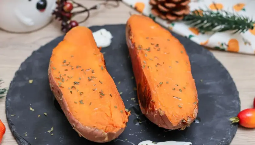 Dos mitades de boniato al horno, tiernas y doradas, espolvoreadas con hierbas, acompañadas de una cremosa salsa.
