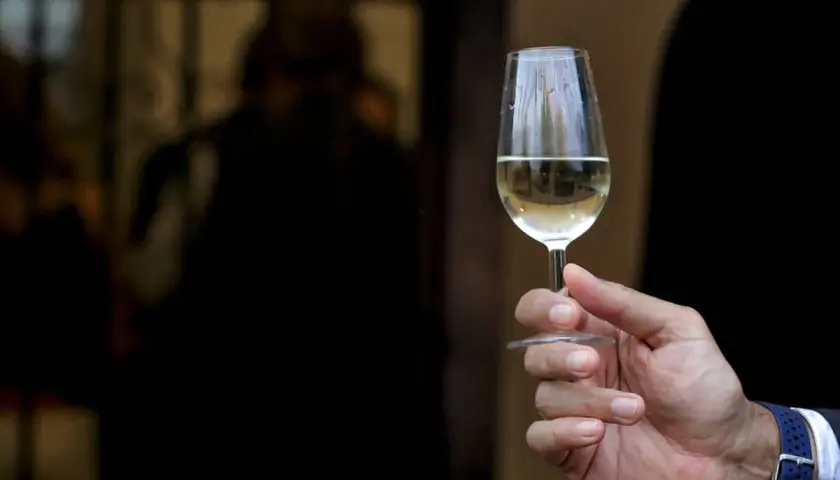 Mano sostiene copa de vino fino y manzanilla, con reflejos en el cristal.