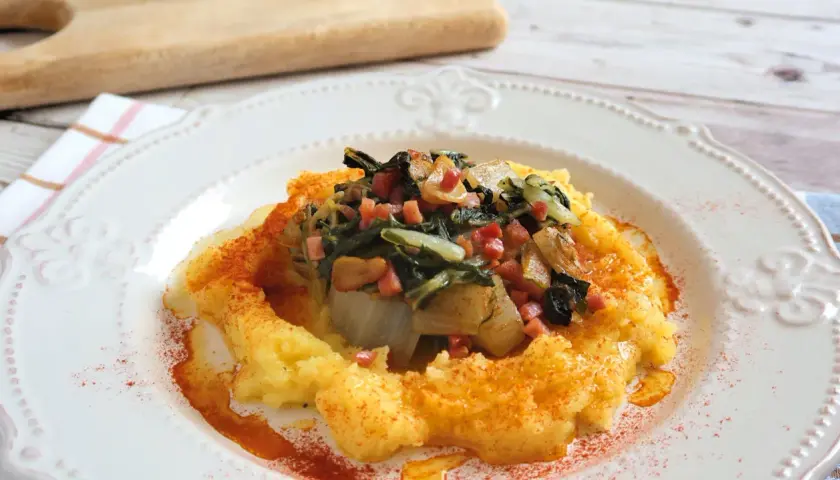 Puré cremoso de patatas con un sofrito de acelgas y trocitos de jamón, espolvoreado con pimentón.