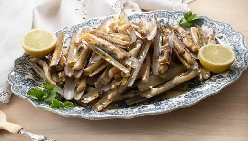 Deliciosas navajas a la plancha servidas en una fuente con limón y perejil.
