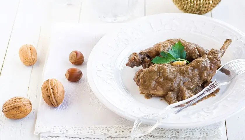 Delicioso conejo al ajillo servido en un plato blanco, acompañado de nueces y avellanas.