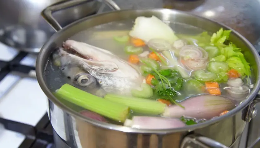 Cabeza de pescado y verduras hirviendo en una olla para hacer un delicioso caldo de pescado casero.