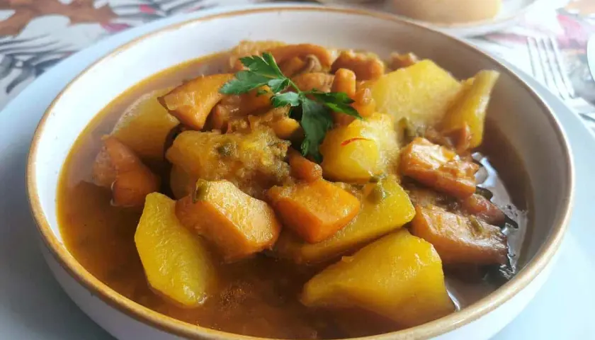 Un reconfortante plato de sepia con patatas, trozos de patata y zanahoria en una sabrosa salsa, adornado con perejil fresco.