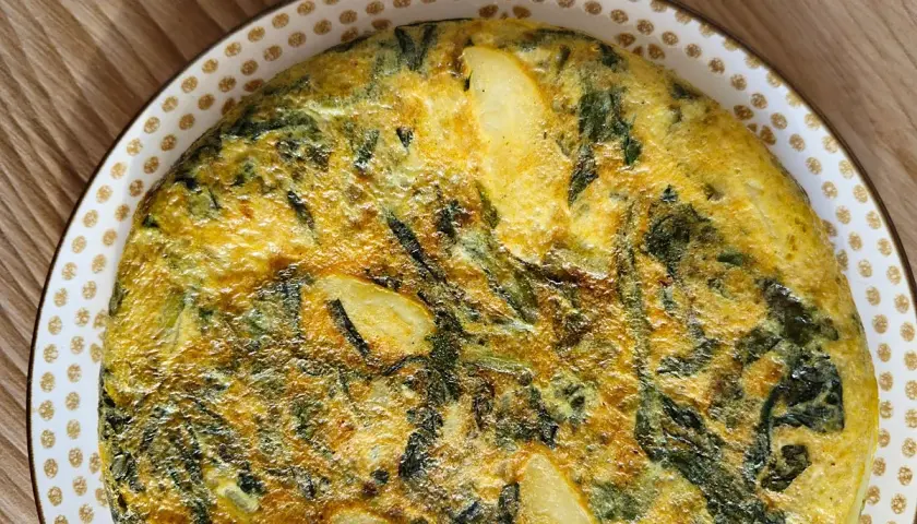 Tortilla de acelgas casera, dorada y jugosa, con trozos de patata y hojas verdes integradas en el huevo.