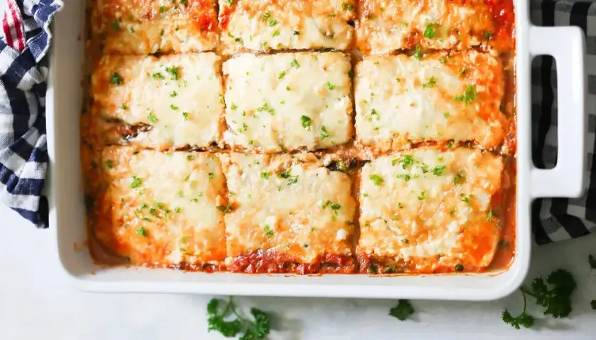 Lasaña de berenjena recién horneada, cubierta de queso derretido y perejil fresco, lista para servir.