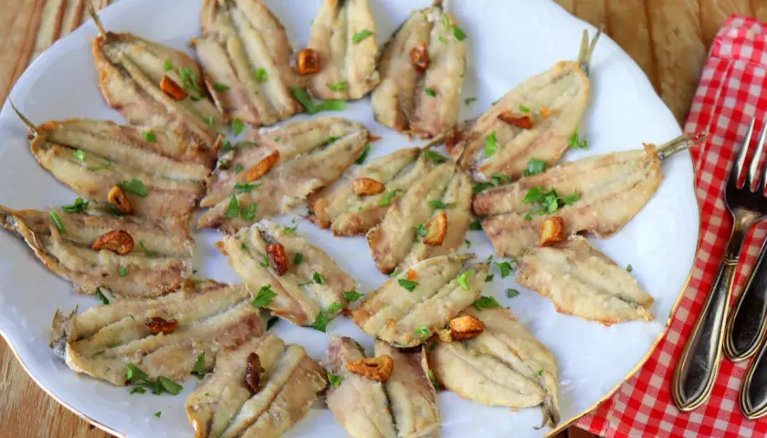 Boquerones en freidora de aire, dorados y crujientes, servidos en plato blanco con perejil picado y ajos fritos. ¡Un manjar saludable!