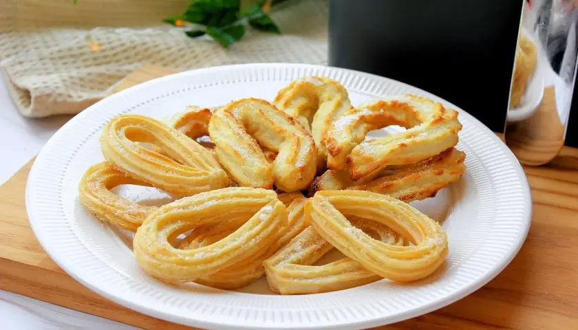 Plato blanco con churros caseros dorados y espolvoreados con azúcar. Perfectos para un antojo dulce.