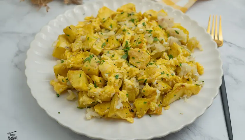 Un delicioso revuelto de bacalao con patatas, espolvoreado con perejil fresco. Un plato casero perfecto para cualquier momento del día.