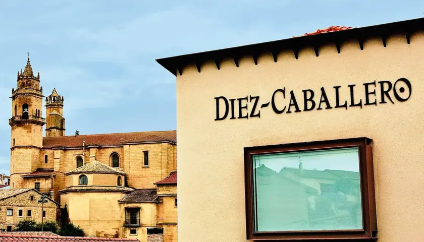 Edificio con el nombre "Diez-Caballero" en relieve, con una iglesia antigua al fondo.