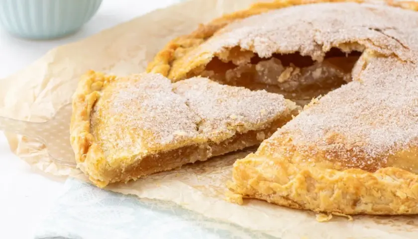 Un delicioso pastel cordobés, espolvoreado con azúcar, con una porción cortada mostrando su relleno dorado.