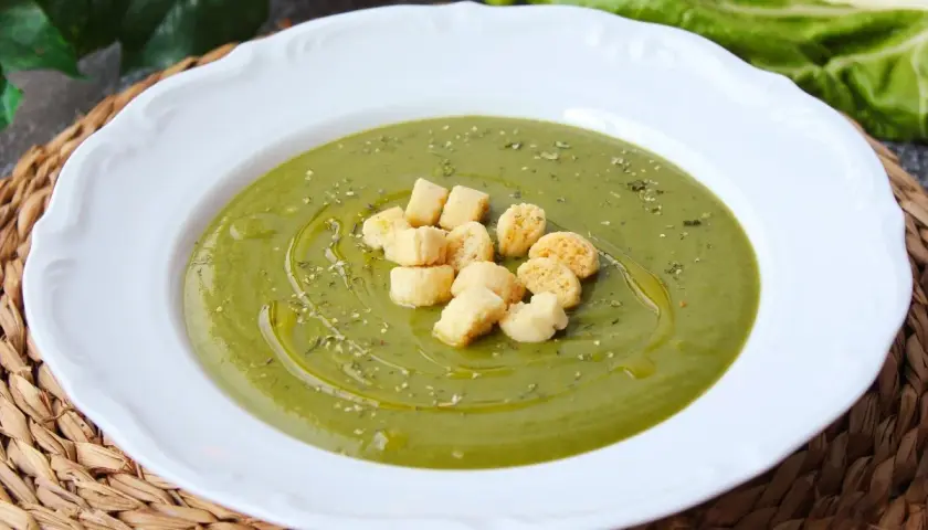 Crema de acelgas verde vibrante, servida en plato blanco con picatostes dorados y un chorrito de aceite de oliva.