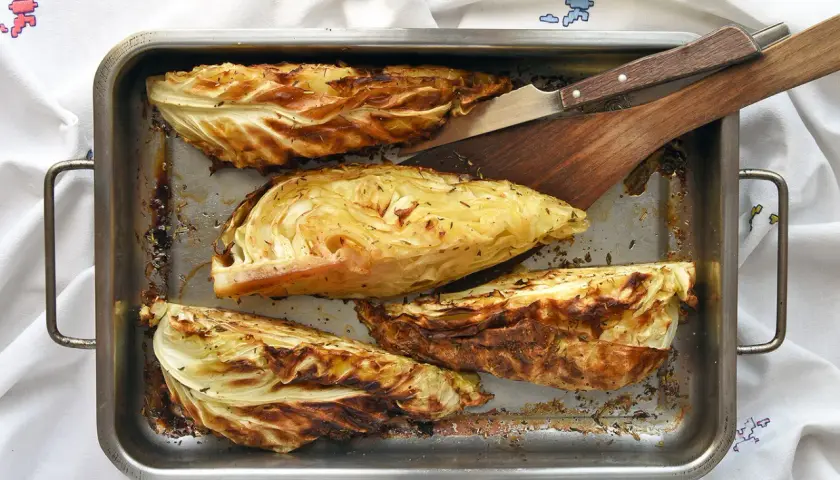 Cuatro gajos de col asada en una bandeja metálica, con hierbas y bordes dorados. Perfectas para tus recetas con col.