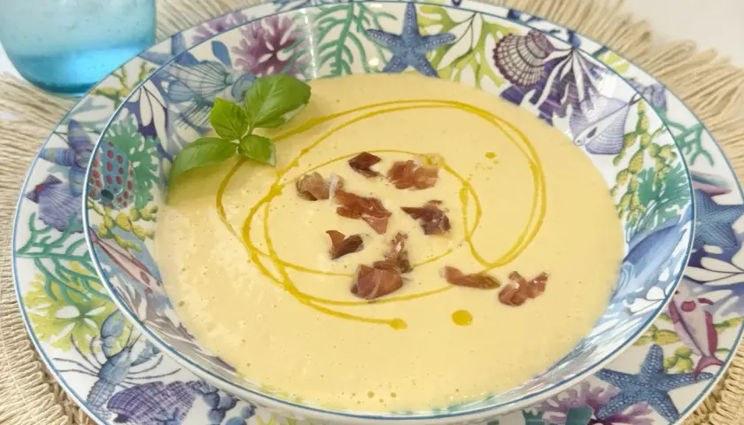 Deliciosa crema de espárragos, coronada con crujientes trocitos de jamón y un hilo de aceite de oliva. Servida en un plato con motivos marinos.