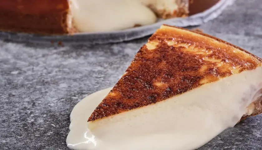 Una porción de tarta de queso cremosa, con la base dorada y el relleno blanco, se desliza sobre una salsa de queso.