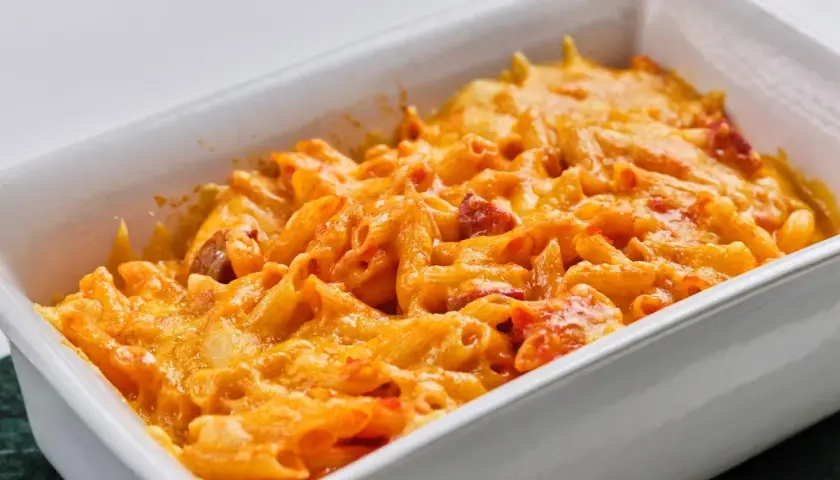 Macarrones con chorizo gratinados, cubiertos de queso derretido y burbujeante en una fuente blanca.