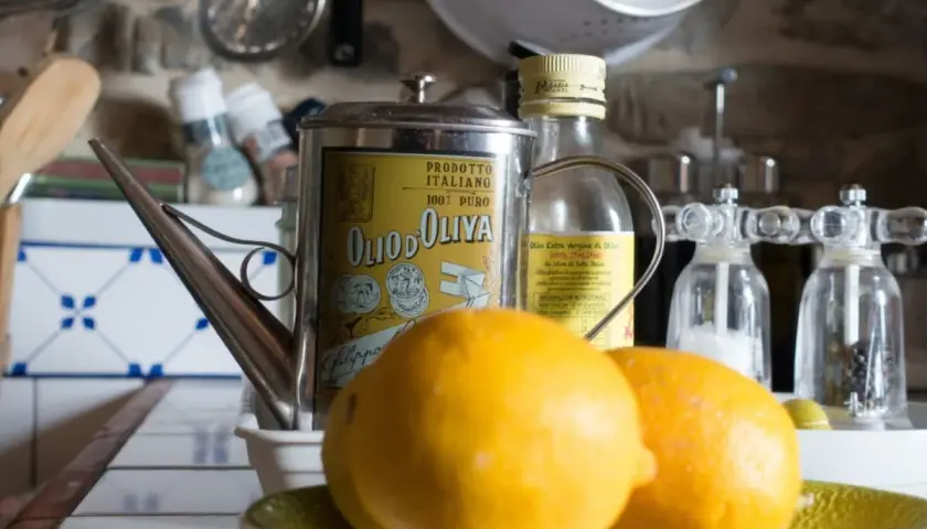 Aceite de oliva y limón para que sirve: una lata vintage de aceite de oliva italiano, limones frescos y molinillos de sal y pimienta en una cocina rústica.