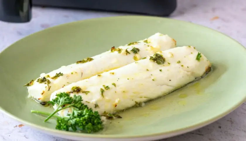 Dos filetes de merluza jugosa, recién hechos en airfryer, con hierbas frescas y aceite de oliva.