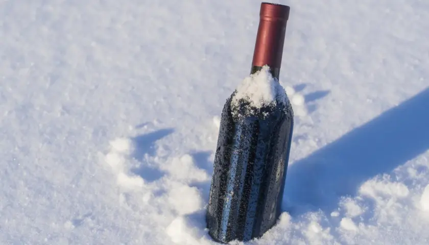 Botella de vino tinto cubierta de nieve, parece que el vino se congela en la nieve.