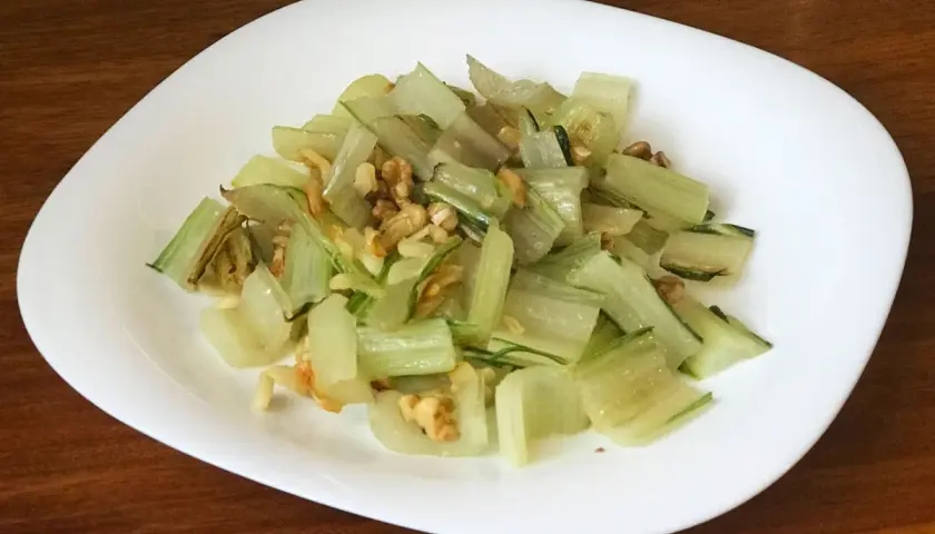 Pencas de acelgas salteadas con nueces, servidas en un plato blanco sobre una mesa de madera.