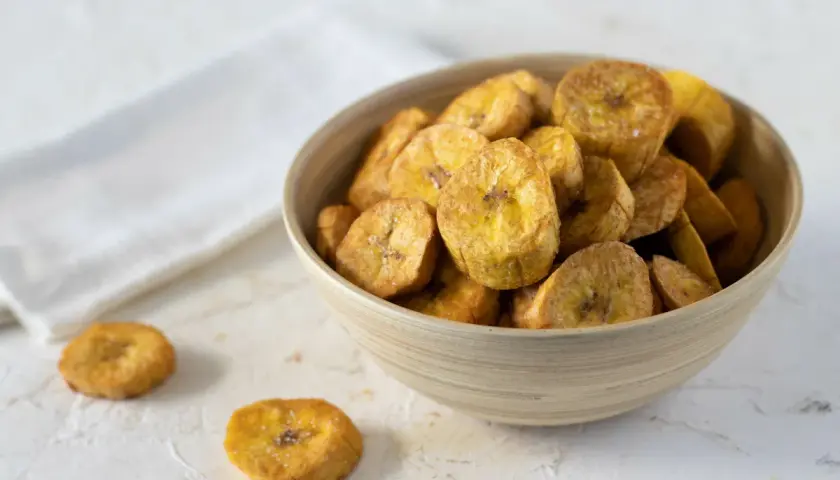 Un tazón de crujientes rodajas de plátano frito, espolvoreadas con sal, listas para disfrutar.