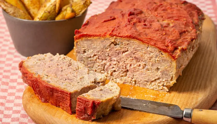Un delicioso pastel de carne picada cubierto de salsa de tomate, servido con patatas gajo.