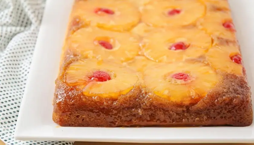 Tarta de piña dorada y brillante, con rodajas de piña caramelizada y cerezas rojas en cada centro. Un postre casero irresistible.