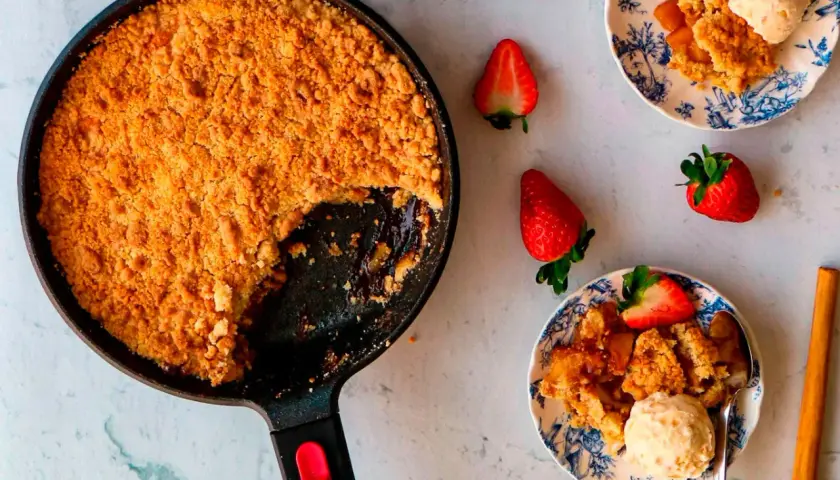 Crumble de manzana recién horneado en sartén, servido en platos con fresas y helado. ¡Un postre casero irresistible!