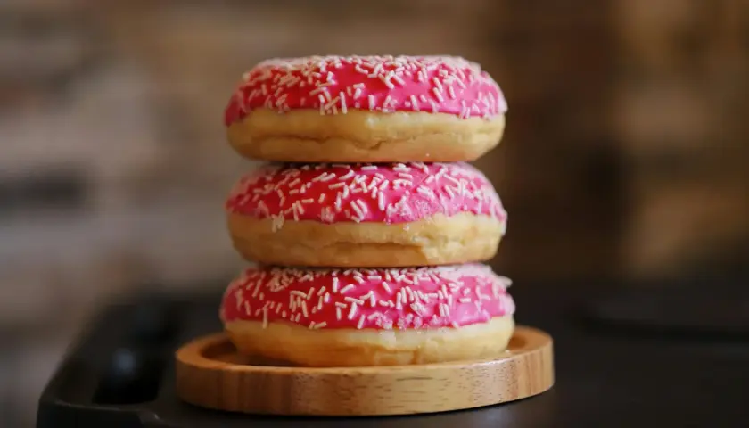 Tres deliciosos donuts caseros apilados, cubiertos con glaseado rosa brillante y chispas blancas.