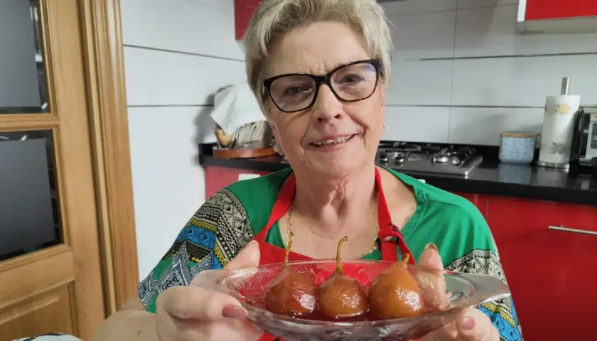 Mujer sonriente muestra un plato con peras al vino, un postre casero listo para disfrutar.