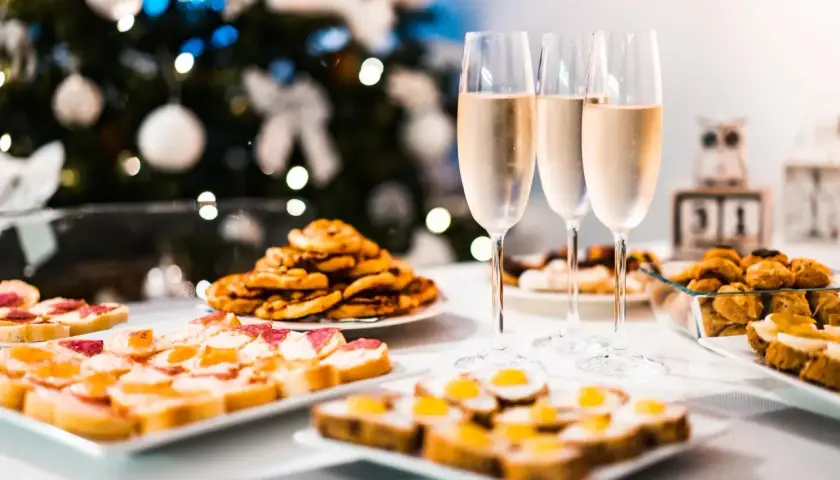 Copas de vino frizzante listas para brindar junto a aperitivos festivos, con un árbol de Navidad decorado al fondo.