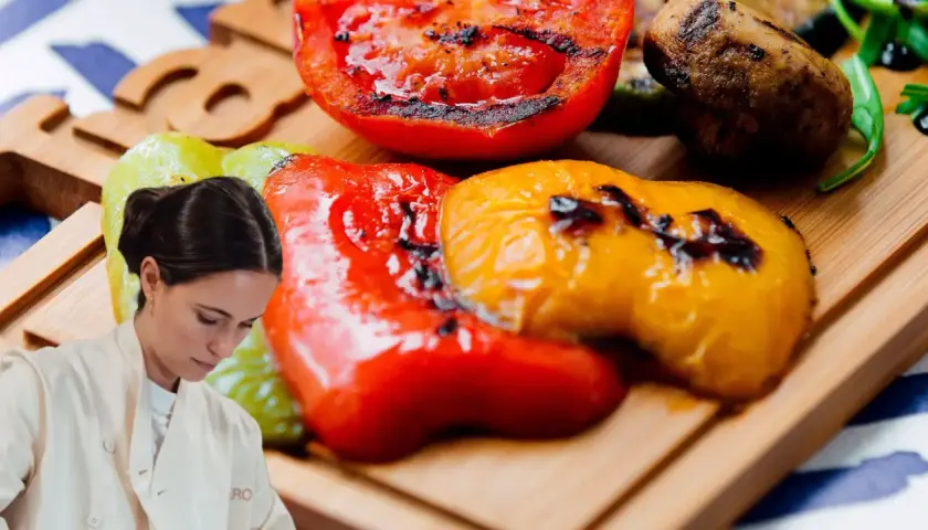 Chef preparando pimientos asados, tomates y champiñones a la parrilla en una tabla de madera.