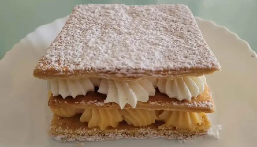 Delicioso milhojas de crema, con capas crujientes de hojaldre y rellenos de crema pastelera y nata montada, espolvoreado con azúcar glas.