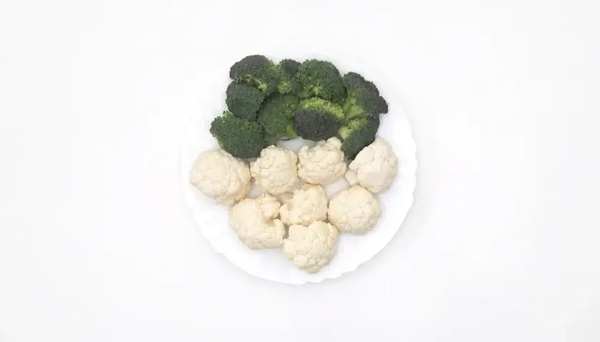 Un plato blanco con un panache de verduras: brócoli verde y coliflor blanca, listos para cocinar.
