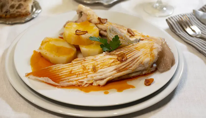 Raya a la gallega servida con patatas cocidas y un toque de ajo frito.