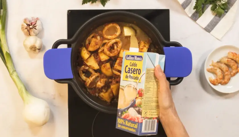 Se añade caldo de pescado a una cazuela con calamares y patatas, ingredientes para una deliciosa caldereta.