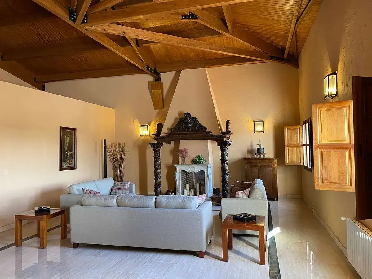 Salón acogedor en finca Los Aljibes, con chimenea rústica, sofás cómodos y vigas de madera en el techo.