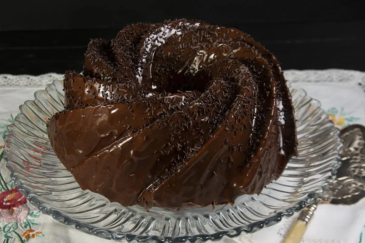 Bizcocho de chocolate glaseado y cubierto con chispas de chocolate, servido en un plato de cristal.