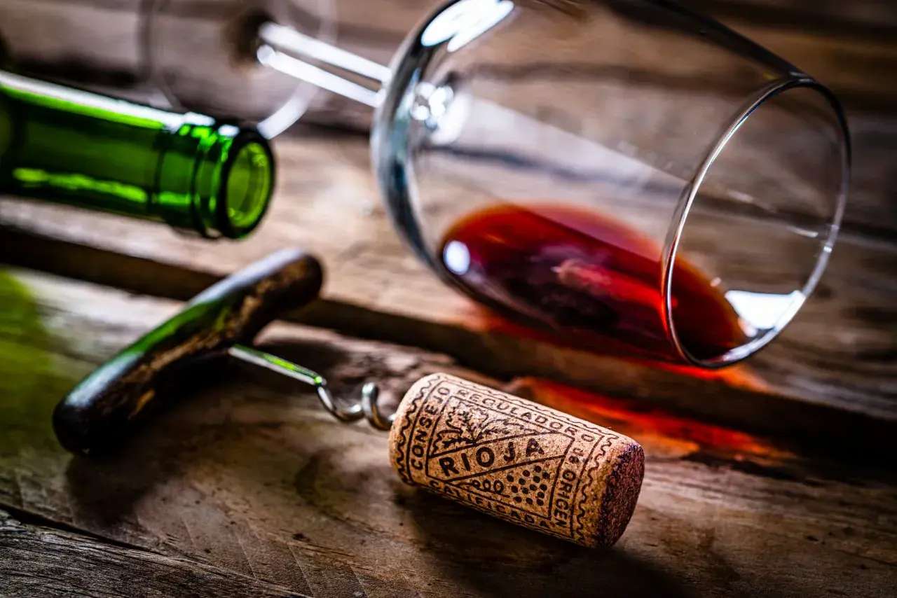 Tapón de corcho con la inscripción "Rioja" y "Calificación Añada", junto a una botella y copa de vino tinto sobre madera.