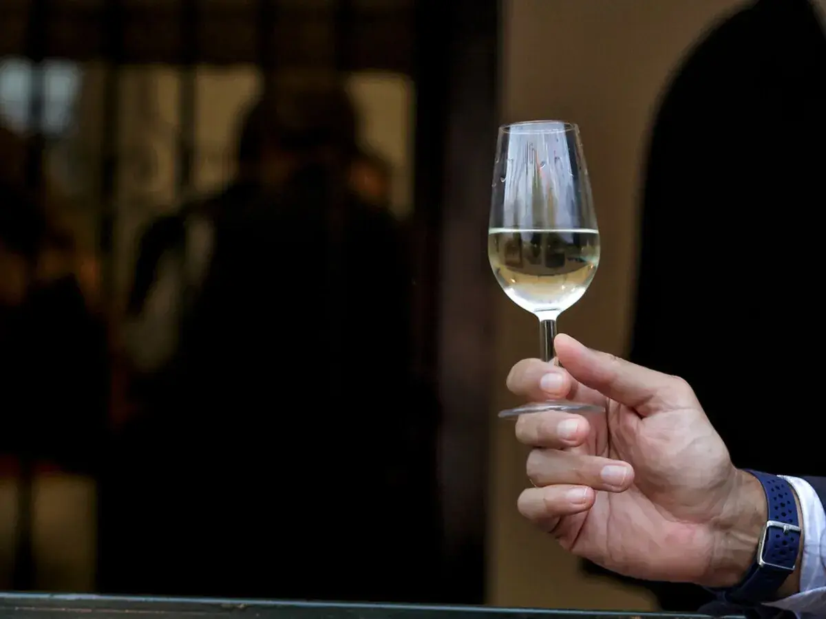 Mano sostiene copa de vino fino y manzanilla, con reflejos en el cristal.
