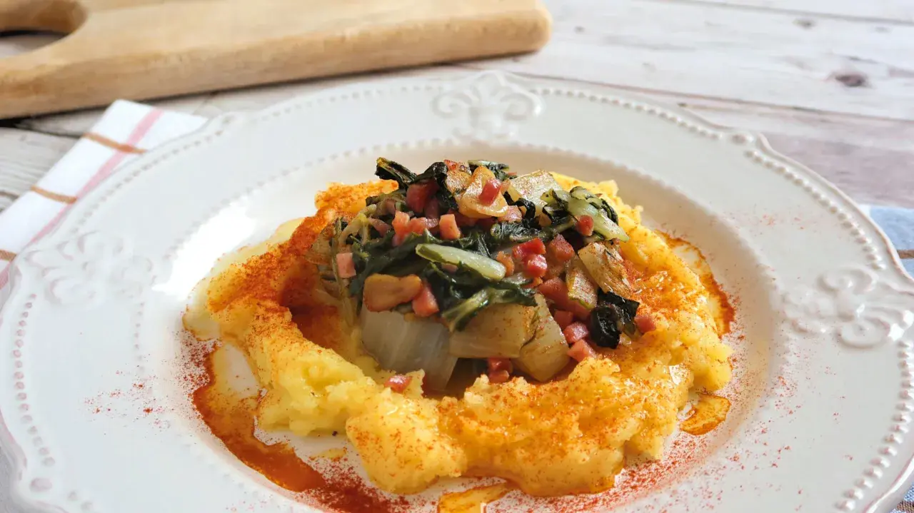Puré cremoso de patatas con un sofrito de acelgas y trocitos de jamón, espolvoreado con pimentón.