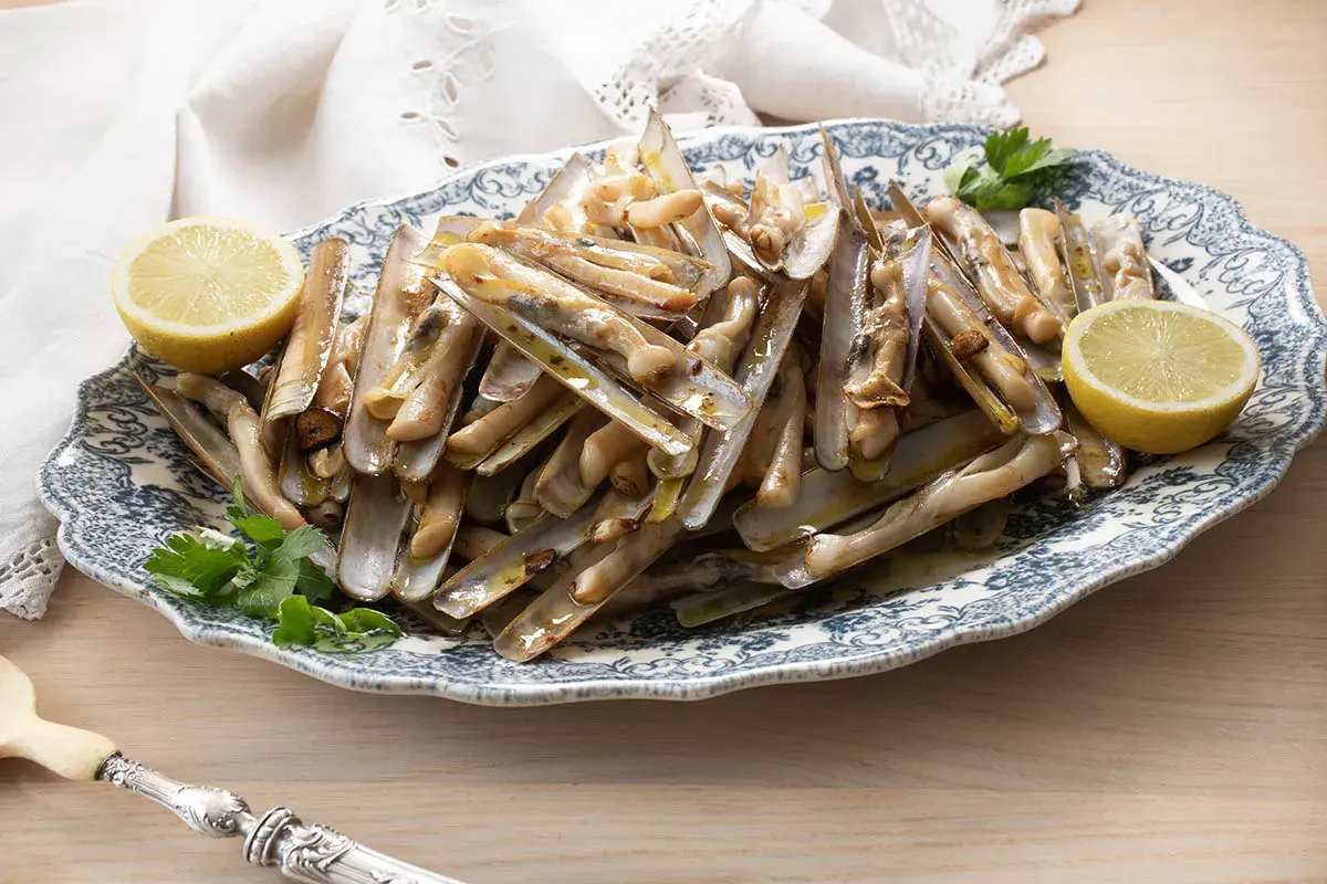 Deliciosas navajas a la plancha servidas en una fuente con limón y perejil.