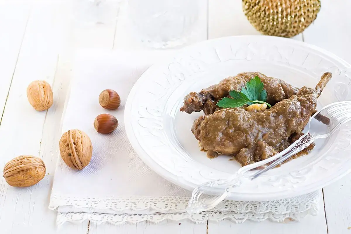 Delicioso conejo al ajillo servido en un plato blanco, acompañado de nueces y avellanas.