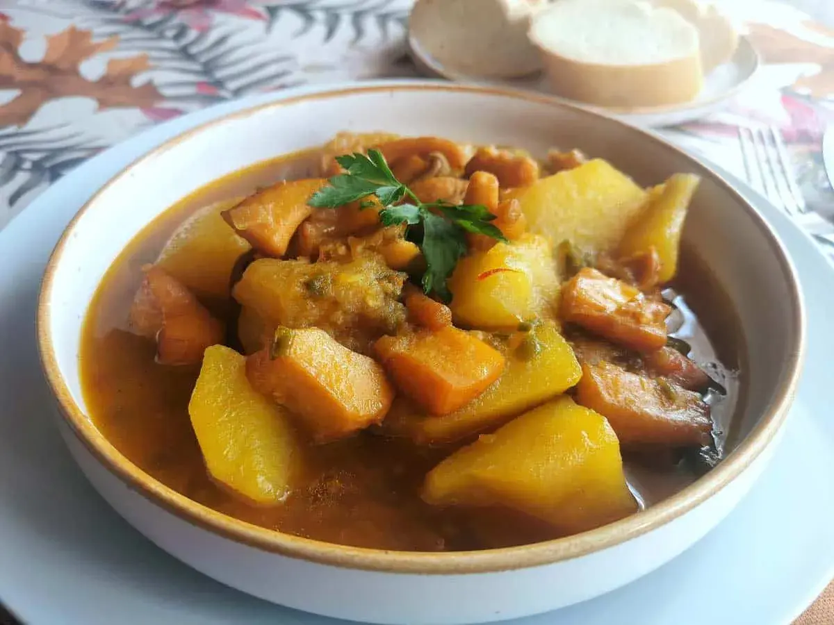 Un reconfortante plato de sepia con patatas, trozos de patata y zanahoria en una sabrosa salsa, adornado con perejil fresco.
