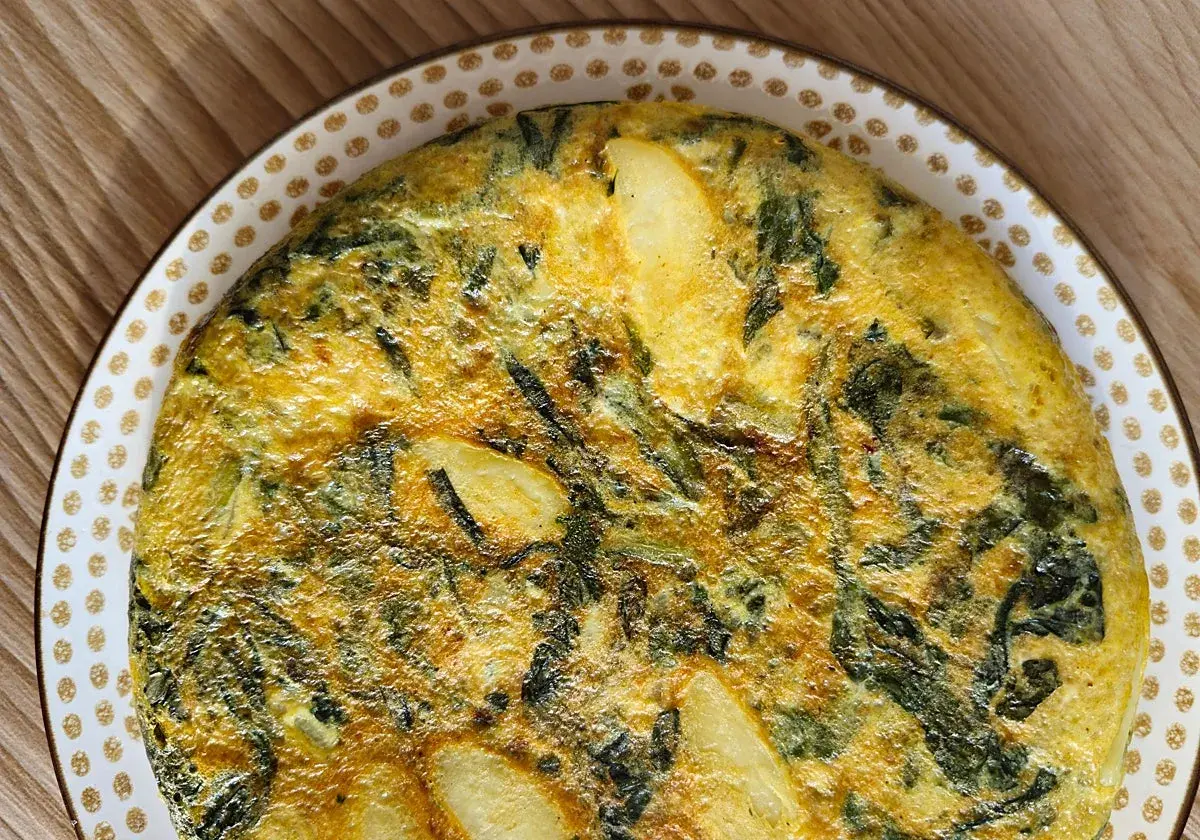 Tortilla de acelgas casera, dorada y jugosa, con trozos de patata y hojas verdes integradas en el huevo.