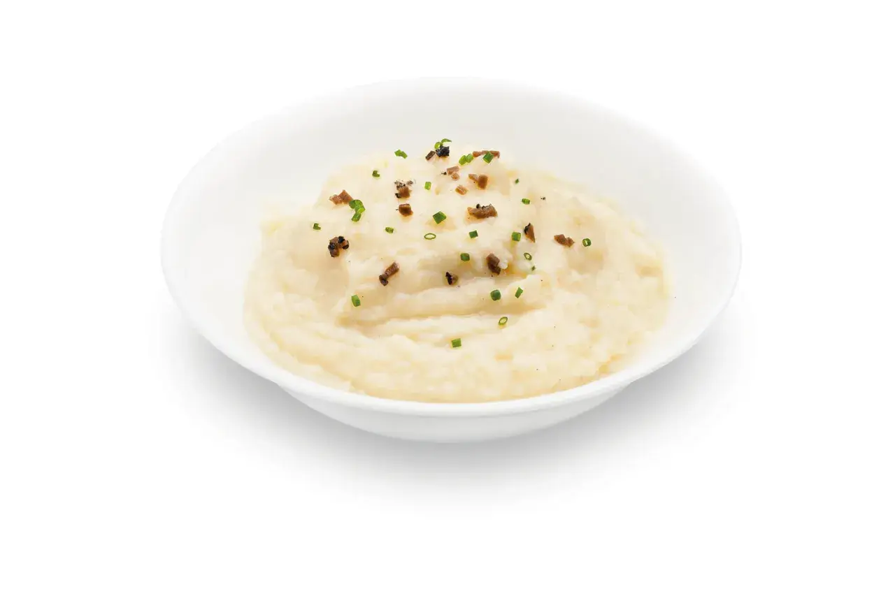 Un cremoso parmentier de patata, adornado con trocitos de bacon crujiente y cebollino fresco.
