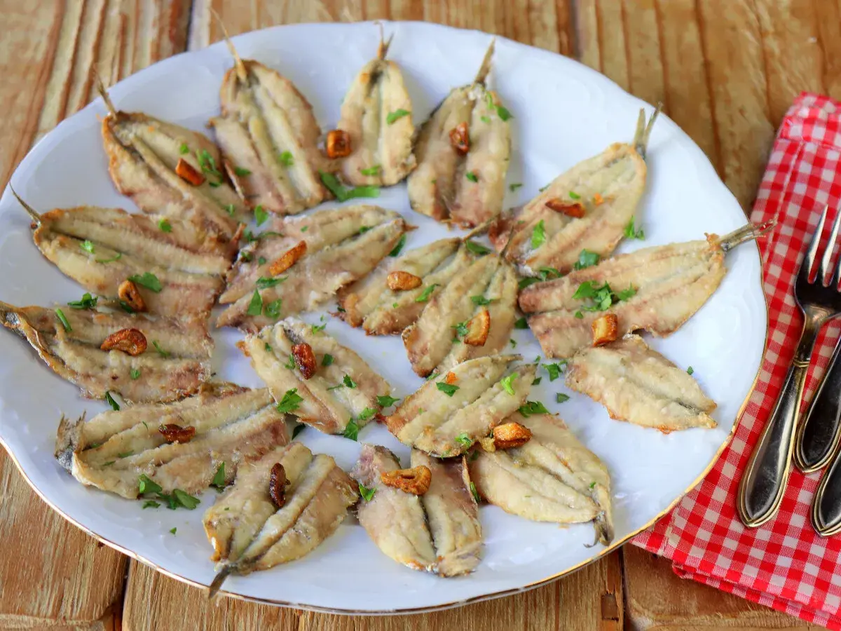 Boquerones en freidora de aire, dorados y crujientes, servidos en plato blanco con perejil picado y ajos fritos. ¡Un manjar saludable!