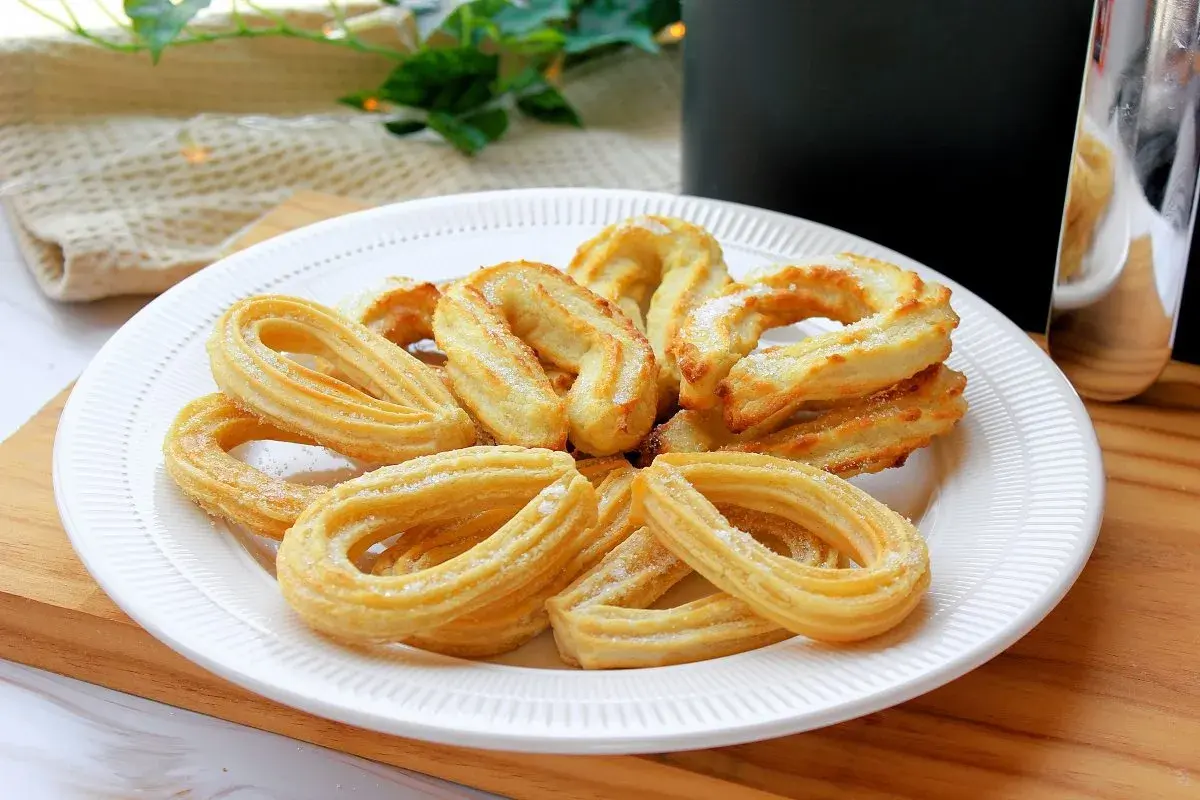 Plato blanco con churros caseros dorados y espolvoreados con azúcar. Perfectos para un antojo dulce.