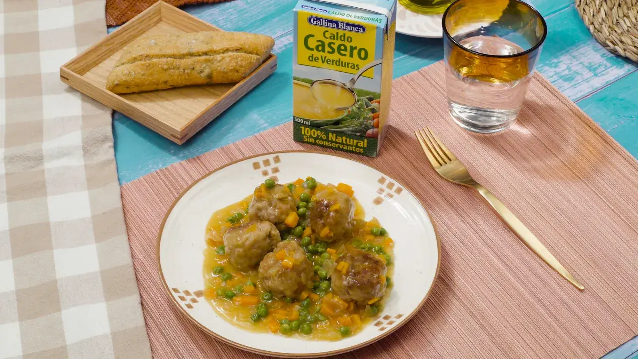 Albondigas a la jardinera en salsa con guisantes y zanahoria, acompañadas de pan y caldo de verduras.