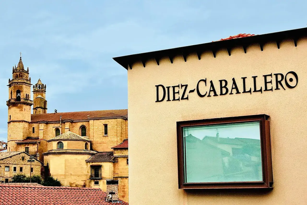 Edificio con el nombre "Diez-Caballero" en relieve, con una iglesia antigua al fondo.